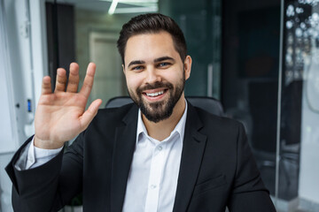 Portrait of smiling male Caucasian boss sit at office desk greeting look at camera in modern office, happy man worker millennial businessman posing, having video call with client or customer online