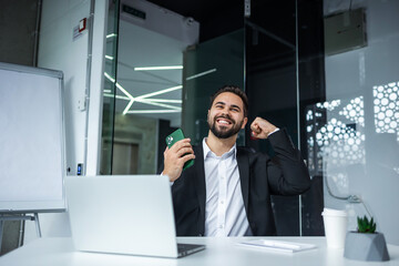 Overjoyed happy millennial business man win using smartphone excited amazed about mobile bet win celebrate victory concept, read great news sit at office desk - 775084341