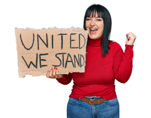 Young hispanic woman holding united we stand banner screaming proud, celebrating victory and success very excited with raised arms