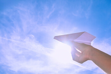 hand holding white paper plane against bright sky - 775086389