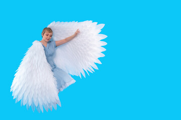 middle age woman in blue dress with big angel wings sitting in the studio on blue background