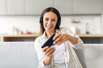 Woman laughing with headphones and phone, playing video game