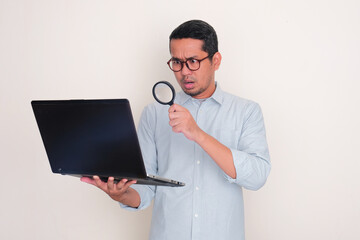 A man looking a laptop screen through magnifying glass with shocked expression