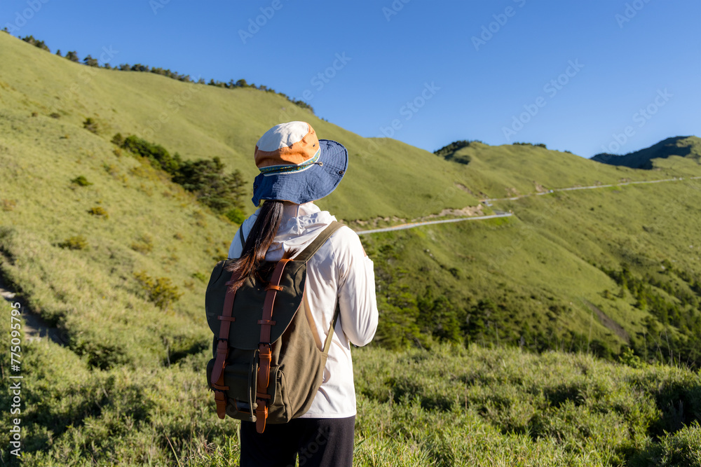 Wall mural girl on mountain peak with green grass looking at beautiful mountain valley