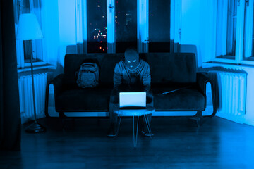 Masked burglar checking laptop in blue light