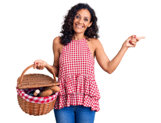 Middle age beautiful woman holding picnic basket with food smiling happy pointing with hand and finger to the side
