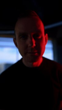 Mid-aged Caucasian man wearing black t-shirt stands in front of camera. Man in the room with flashing light tilting head from side to side. Close up. Vertical video.