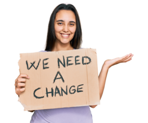 Young hispanic woman holding we need a change banner celebrating victory with happy smile and winner expression with raised hands