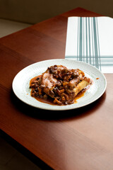 Braised Pork's Trotters with Mushrooms on Empty Wooden Table- Traditional Catalan Cuisine in a Rustic Restaurant Ambiance.