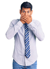 Young latin man wearing business clothes shocked covering mouth with hands for mistake. secret concept.