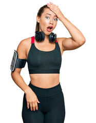 Beautiful blonde woman wearing gym clothes and using headphones surprised with hand on head for mistake, remember error. forgot, bad memory concept.