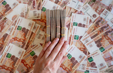 Russian banknotes in denomination of five thousand Russian rubles and bundles of money against the background of ruble bills and a hand holding bundles of money - obrazy, fototapety, plakaty