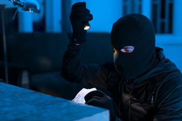 Thief stealing money with flashlight in dark setting