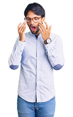 Handsome hispanic man wearing business shirt and glasses rubbing eyes for fatigue and headache,...