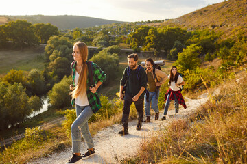 Group of young happy smiling people tourists with large backpacks hiking in nature walking in a row. Cheerful active friends trekking outdoors. Adventure, travel and tourism concept.