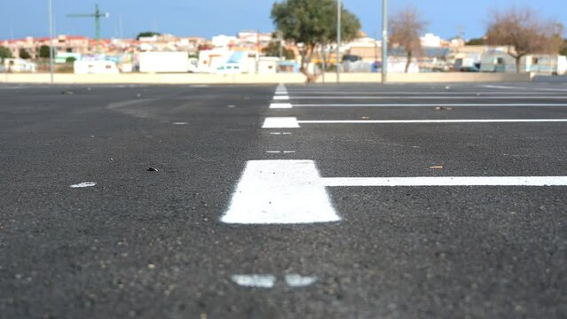 Marking on new asphalt for parking spaces with white paint in a parking lot with a city in the background and blue sky.