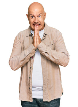 Middle age bald man wearing casual clothes praying with hands together asking for forgiveness smiling confident.