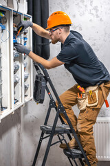 A male electrician works in a switchboard with an electrical connecting cable.