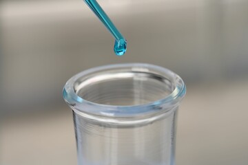 Laboratory analysis. Dripping blue liquid into flask on blurred background, closeup