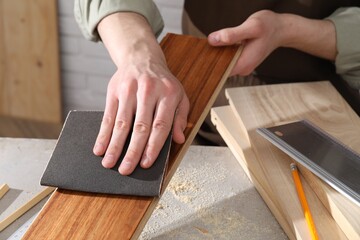 Fototapeta na wymiar Man polishing wooden plank with sandpaper at grey table indoors, closeup