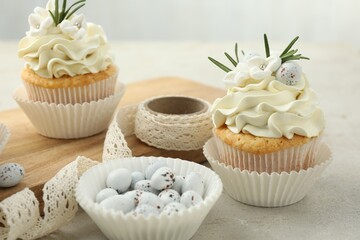 Tasty Easter cupcakes with vanilla cream, candies and ribbon on gray table, closeup