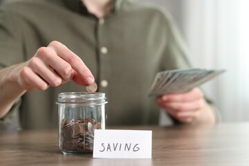 Fototapeta premium Financial savings. Man putting coin into glass jar at wooden table, closeup