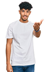 Obraz premium Young arab man wearing casual white t shirt smiling friendly offering handshake as greeting and welcoming. successful business.