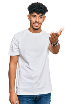 Naklejki Young arab man wearing casual white t shirt smiling friendly offering handshake as greeting and welcoming. successful business.