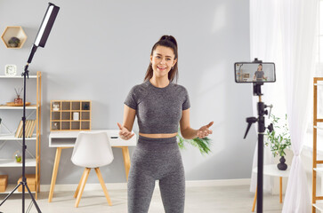 Sporty athlete young woman fitness instructor in sportswear recording video of online training in mobile phone camera. Slim girl blogger talking about sport workout making video for fitness blog - obrazy, fototapety, plakaty