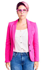 Young beautiful woman with pink hair wearing business jacket and glasses with serious expression on face. simple and natural looking at the camera.