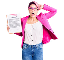 Young beautiful woman with pink hair holding clipboard with contract document crazy and scared with hands on head, afraid and surprised of shock with open mouth