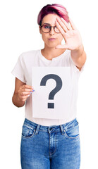 Young beautiful woman with pink hair holding question mark with open hand doing stop sign with serious and confident expression, defense gesture