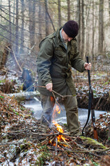 The hunter puts thin dry branches on the fire