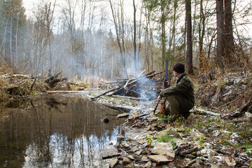 The hunter sat down by the campfire on the bank of the forest river