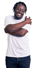 Young african american man with braids wearing casual white tshirt hugging oneself happy and positive, smiling confident. self love and self care