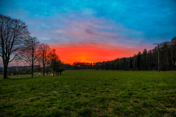 Fototapeta na wymiar Bright red sunset Over meadows at the edge of a forest next to a road near Koblenz