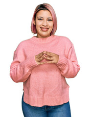 Hispanic woman with pink hair wearing casual winter sweater hands together and fingers crossed smiling relaxed and cheerful. success and optimistic