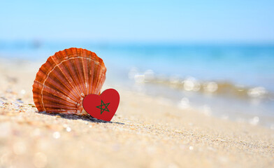 Sandy beach in Morocco. Moroccan flag in the shape of a heart and a large shell. A wonderful...
