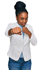 Young african american woman wearing business clothes punching fist to fight, aggressive and angry attack, threat and violence
