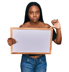 Young african american woman holding empty white chalkboard with angry face, negative sign showing...