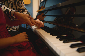 Side view of a music teacher, musician pianist holding the hands of a child girl, teaching piano,...