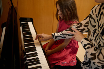 Little kid girl in elegant red dress, taking piano lesson, passionately playing the keys under her...