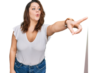 Young plus size woman wearing casual white t shirt pointing with finger surprised ahead, open mouth amazed expression, something on the front