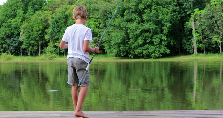 Young boy fishing at pristine beautiful green lake in outdoor nature