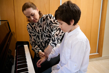 Handsome teenage boy taking piano lesson, passionately playing the keys under her teacher's...