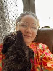 Happy female person hugging black poodle puppy at home. Peaceful girl holding brown dog. Vintage style picture of Asian woman embracing puppy. Soft focus. film grain pixel texture. Defocused.