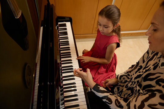 Little child girl having a piano lesson with her teacher. Female pianist explaining the correct position of hands on piano keys.