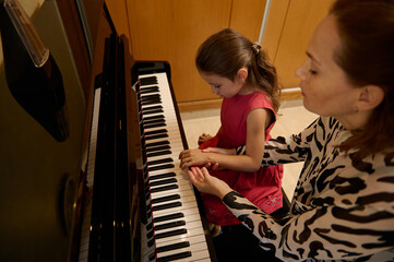 Little child girl having a piano lesson with her teacher. Female pianist explaining the correct...