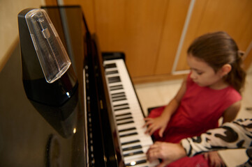Little kid girl having a piano lesson with her teacher at home. Little child girl putting her fingers on ebony and ivory keys, creating rhythm of sound, composing melody and singing Christmas song