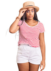 Young african american woman with braids wearing summer hat worried and stressed about a problem with hand on forehead, nervous and anxious for crisis